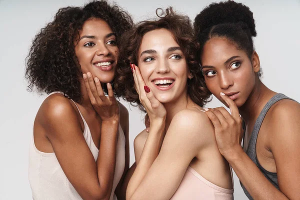 Üç neşeli çoklu etnik kadının portresi beyaz arka planda izole edilmiş bir şekilde gülümsüyor ve yan tarafa bakıyordu.