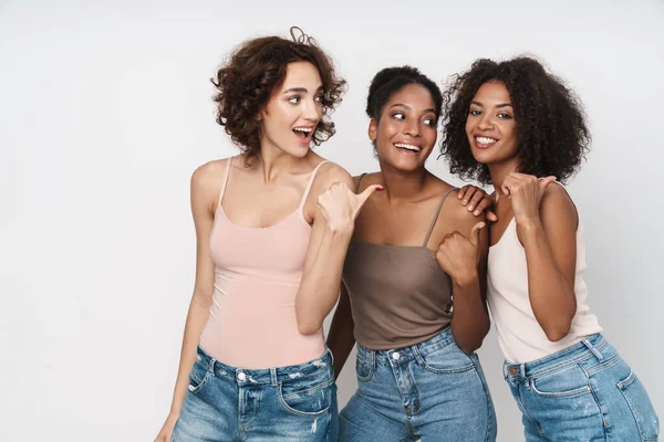 Beyaz arka planda izole edilmiş, gülümseyen ve işaret eden üç güzel kadının portresi.