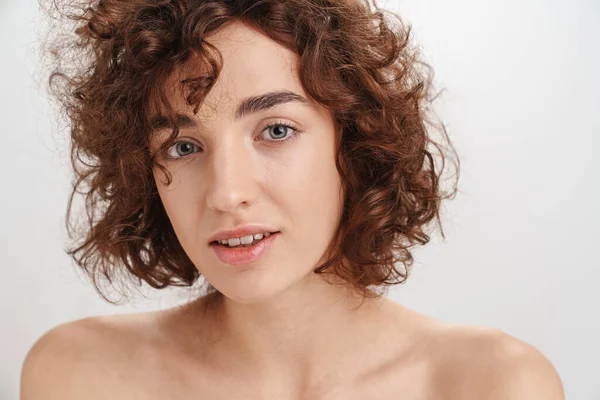 Beyaz arka planda izole edilmiş kısa kıvırcık kahverengi saçlı çekici, üstsüz bir kadının güzel portresi. Kameraya bakıyor.