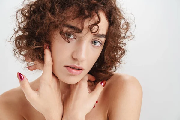 Beyaz arka planda izole edilmiş kısa kıvırcık kahverengi saçlı çekici, üstsüz bir kadının güzel portresi. Kameraya bakıyor.