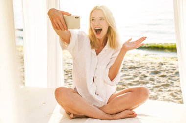 Heyecanlı bir kadının yaz plajında otelde cep telefonuyla selfie çekerken şaşkınlığını ifade etmesi.