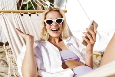 Yazın plajda hamakta uzanırken cep telefonu kullanan çekici, heyecanlı bir kadın.