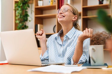 Ofiste dizüstü bilgisayarla çalışırken kazanan jest yapan heyecanlı genç iş kadını görüntüsü