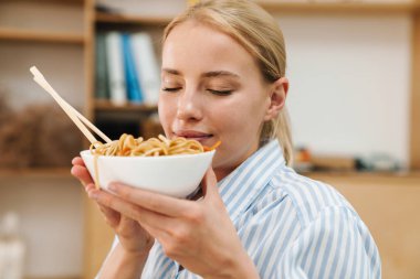 Ofiste çalışırken Asya eriştesi yiyen mutlu sarışın kadın görüntüsü.