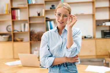 Ofiste kameraya poz veren gözlüklü çekici bir kadın.