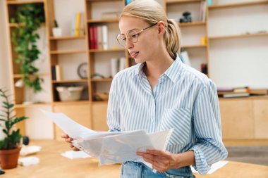 Gözlüklü çekici bir kadının ofiste duran belgeleri incelerkenki görüntüsü