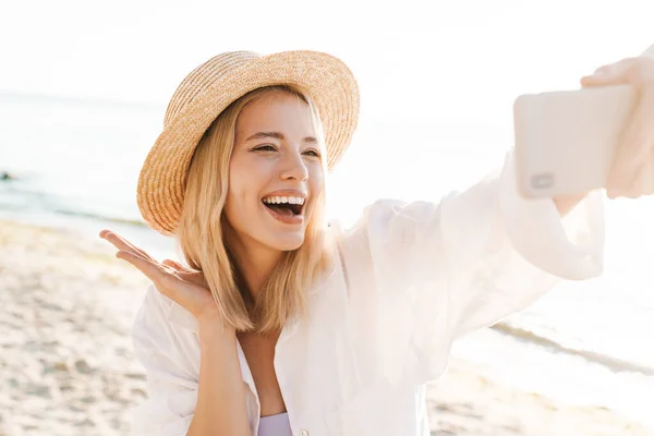 幸せな女性の笑顔のイメージと夏のビーチに立っている間に携帯電話で自撮り写真を撮る — ストック写真