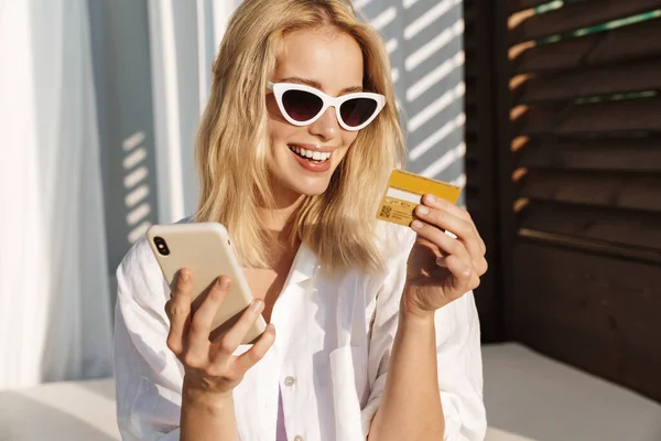 Imagem Mulher Animada Óculos Escuros Segurando Cartão Crédito Usando Celular — Fotografia de Stock