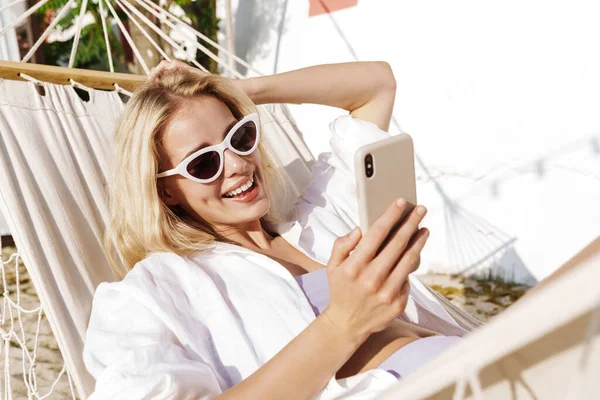 Imagem Mulher Sorridente Encantadora Usando Celular Enquanto Deitado Rede Praia — Fotografia de Stock