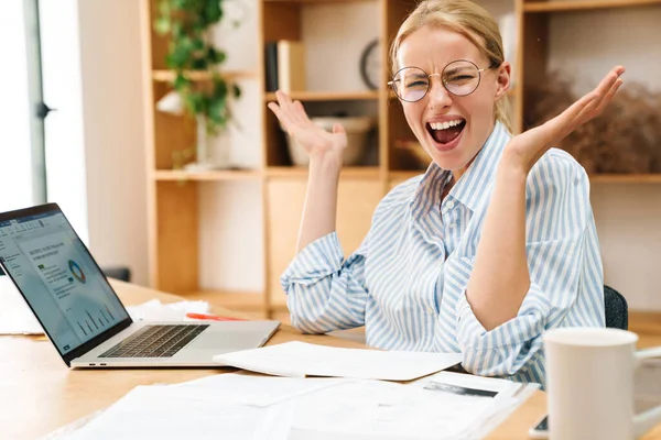 Ofisteki masada laptopla ve kağıtlarla çalışırken bağıran hoşnutsuz sarışın kadın görüntüsü