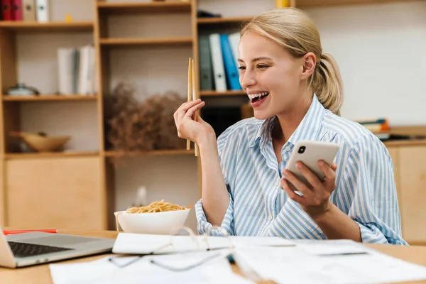 Imagem Mulher Loira Alegre Comendo Macarrão Asiático Enquanto Usa Celular — Fotografia de Stock