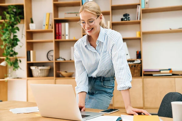 Ofiste otururken dizüstü bilgisayarla gülümseyen ve çalışan mutlu bir kadın resmi.