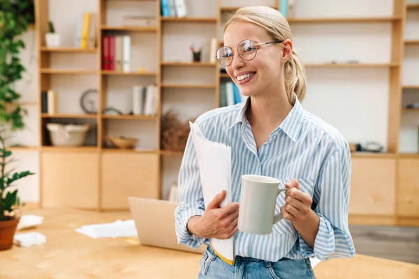 オフィスで紙を振りながら眼鏡をかけコーヒーを飲みながら楽しい魅力的な女性のイメージ — ストック写真