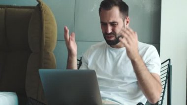 Mutsuz genç bir adam dizüstü bilgisayarını içeride kullanıyor.