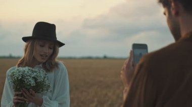 Yakışıklı genç adam tarlada kız arkadaşının fotoğrafını çekiyor.