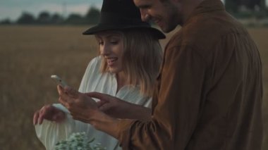 Gülümseyen bir erkek ve kadın cep telefonundaki fotoğrafları izliyorlar.