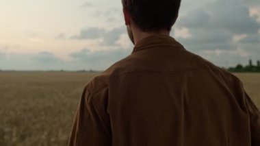 Yakışıklı, rahat genç bir adamın arka planı sahada yürüyor.