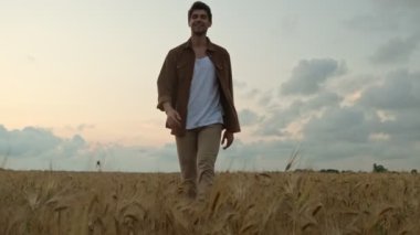 Gülümseyen bir genç adam yaz zamanı sahada yürüyor.