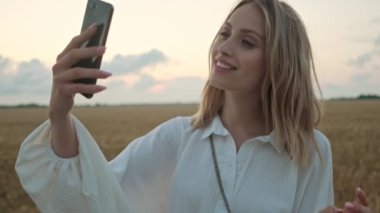 Sarışın güzel bir kadın yazın sahada yürürken selfie çekiyor.