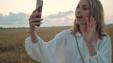 Sarışın, güzel bir kadın yazın sahada yürürken video bağlantısını kullanarak akıllı telefondan konuşuyor.