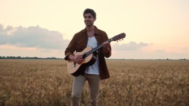 Mutlu bir adam tarlada yürürken gitar çalıyor.