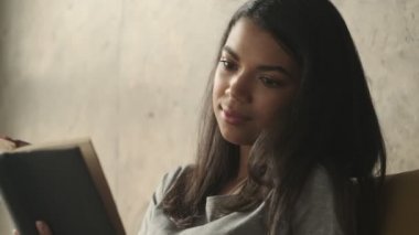 Evde kitap okuyan konsantre genç bir kadın.