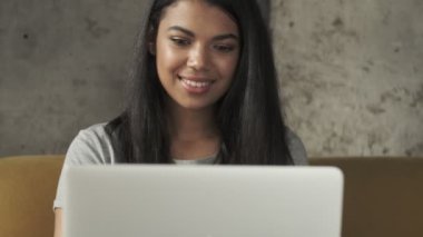 Evde dizüstü bilgisayar kullanan genç, pozitif odaklı bir kadın.