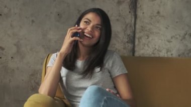 Evde cep telefonuyla konuşan mutlu, genç bir kadın.