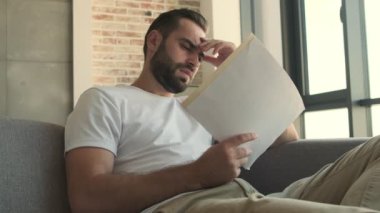 Evde elinde belgelerle oturan sinirli bir genç.