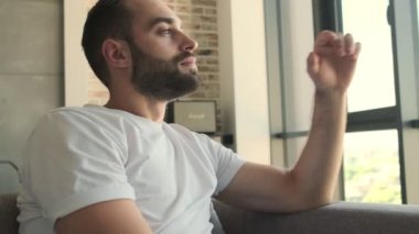 Genç, mutlu, pozitif bir adam evde, kanepede oturuyor.