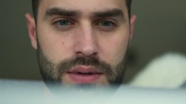 Evde oturup dizüstü bilgisayar kullanan yakışıklı, ciddi bir adamın yakın çekim videosu.