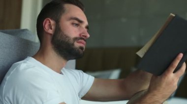 Evde oturup kitap okuyan yakışıklı, ciddi bir adam.