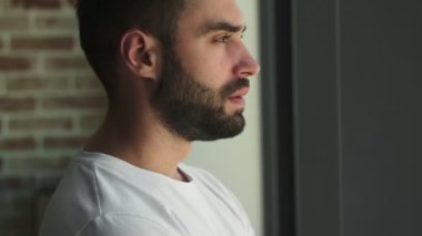 Evdeki pencerenin yanında duran yakışıklı, ciddi bir adam.