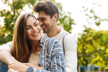 Parkta yürürken gülümseyen ve sarılan Kafkasyalı mutlu esmer çiftin görüntüsü