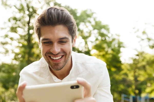 Imagen Joven Caucásico Morena Hombre Sonriendo Sosteniendo Teléfono Celular Mientras — Foto de Stock
