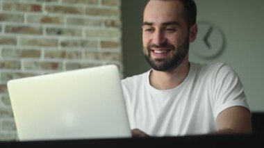 Evde dizüstü bilgisayar kullanan mutlu bir genç.