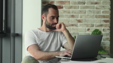 Evde dizüstü bilgisayar kullanan üzgün genç bir adam.