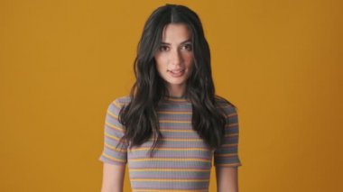 Güzel bir genç kadın gülüyor. Sarı arka planda tek başına duruyor.