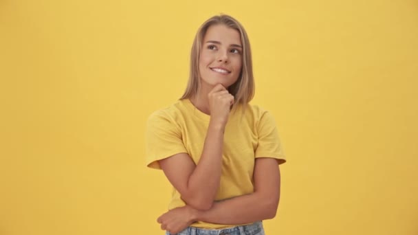魅力的な若いですブロンド女性で黄色のTシャツあります夢を見ています何か立っていることについて黄色の背景 — ストック動画