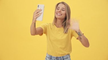Dost canlısı genç bir kadın telefonda konuşuyor. Sarı arka planda tek başına duran video bağlantısını kullanıyor.