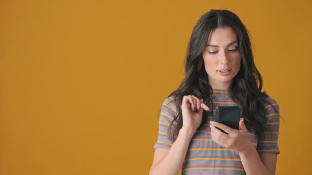 Радостная Молодая Женщина Использует Свой Смартфон Стоящий Изолированно Желтом Фоне — стоковое видео