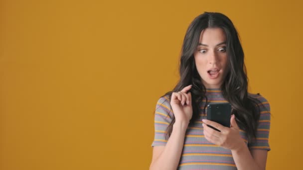 Zdziwiona Młoda Kobieta Używa Swojego Smartfona Wskazując Stronę Stojącą Żółtym — Wideo stockowe