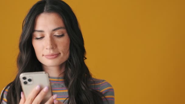 Skupiona Młoda Kobieta Korzystająca Smartfona Stojącego Żółtym Tle — Wideo stockowe