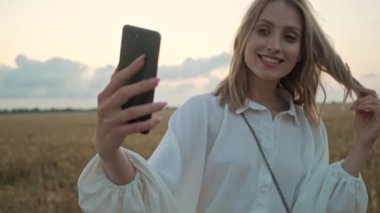 Gülümseyen genç sarışın bir kadın yazın sahada yürürken selfie çekiyor.
