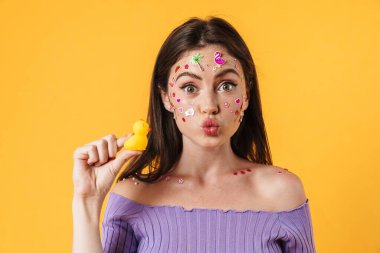 Sarı arka planda plastik ördek tutan yüzü etiketli neşeli genç bir kadın resmi