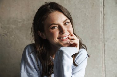 Çekici, neşeli bir kadının evde poz verirken gülümseyen ve kameraya bakan görüntüsü