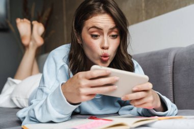 Evdeki kanepede uzanmış, internetten oyun oynayan heyecanlı bir kadın görüntüsü.