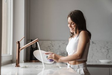Mutfakta bulaşık yıkayan ve gülümseyen beyaz kadın imajı.