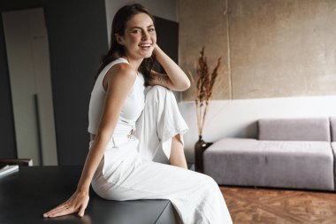 Evdeki oturma odasında gülümseyen ve oturan güzel bir kadın görüntüsü.