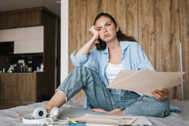 Evde elinde kağıt belgeler tutan yorgun bir kızın resmi.